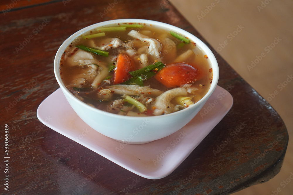 Spicy soup with cartilage in a white plastic bowl on a pink plastic square plate, on wooden table, nature, food, vegetables Spicy soup with cartilage in a white plastic bowl on a pink plastic square plate, on wooden table, nature, food, vegetables