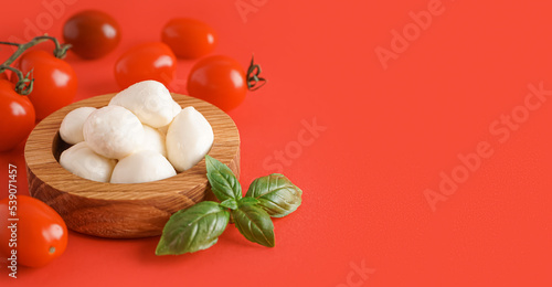 Wooden bowl with delicious mozzarella cheese and tomatoes on red background with space for text