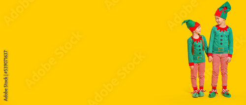 Little children in costumes of elves on yellow background with space for text