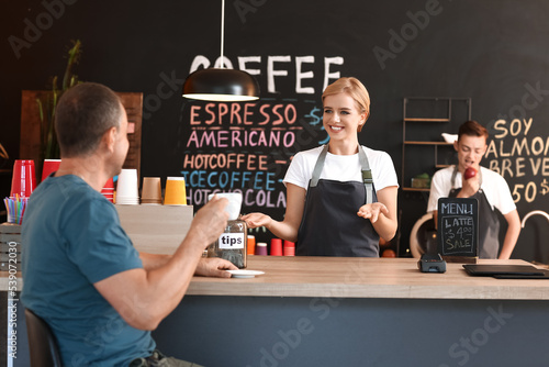 Young female barista and visitor in cafe
