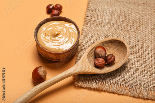 Bowl of tasty nut butter and hazelnuts on color background