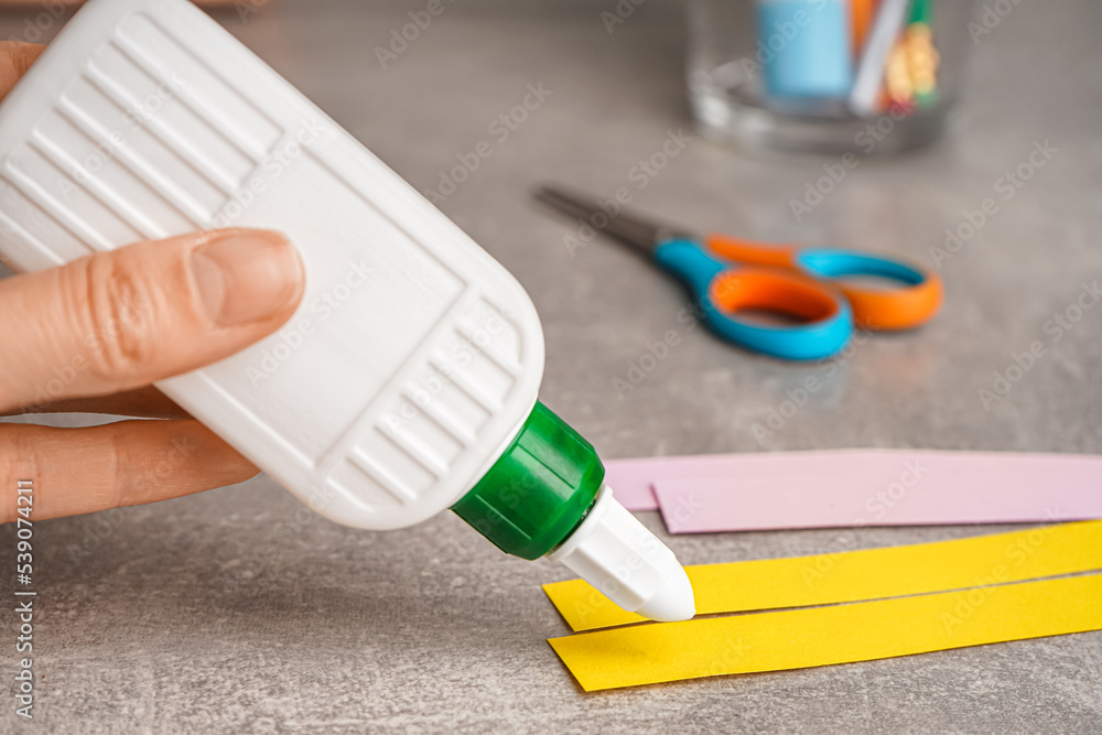 Man with bottle of glue and paper pieces on grunge background, closeup