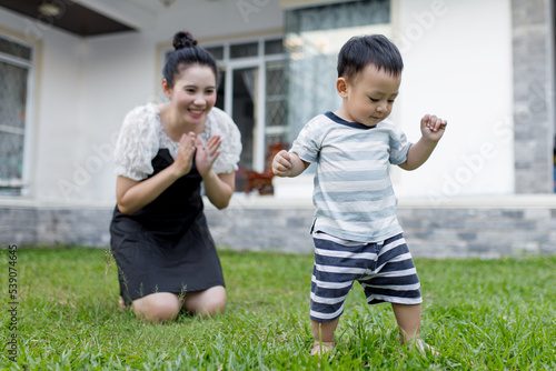 Quadro em tela The first step little baby learning to walk with a happy mother in the front yard