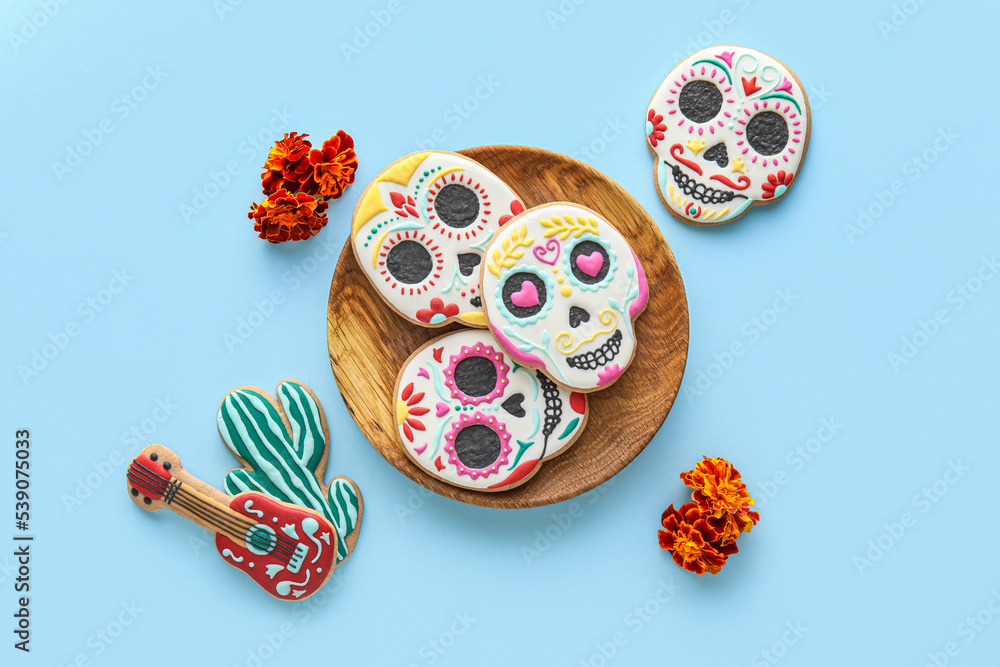 Plate with tasty cookies and flowers on blue background. El Dia de Muertos