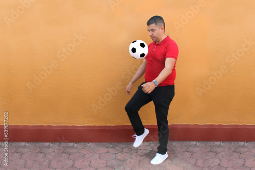 Fototapeta Naklejka Na Ścianę i Meble -  Latino adult man plays with a soccer ball very excited that he is going to see the World Cup and wants to see his team win