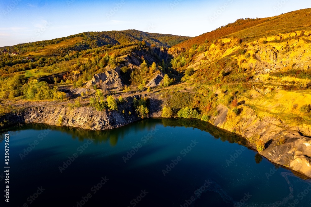 Aerial view of a small lake at sunset, that formed in a former coal mine exploitation, near Resita city, Romania. Captured with a drone, from above, in autumn setting.
