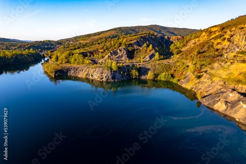 Aerial view of a small lake at sunset, that formed in a former coal mine exploitation, near Resita city, Romania. Captured with a drone, from above, in autumn setting. 