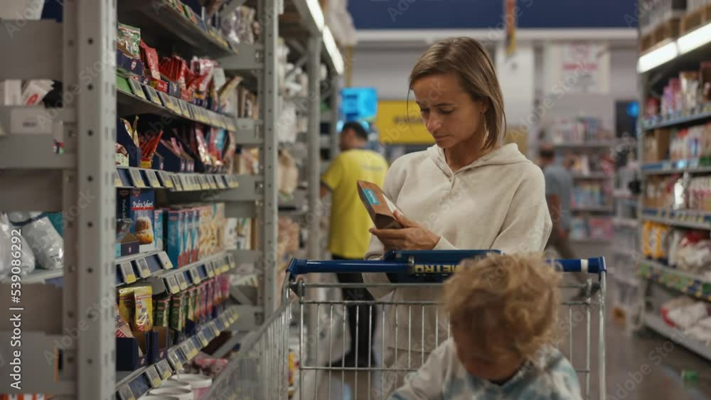 The girl the buyer chooses products in on the shelves of the supermarket. The buyer examines the product of the jar of canned food. A hand picks up a product from a store shelf. The girl the buyer chooses products in on the shelves of the supermarket. The buyer examines the product of the jar of canned food. A hand picks up a product from a store shelf.