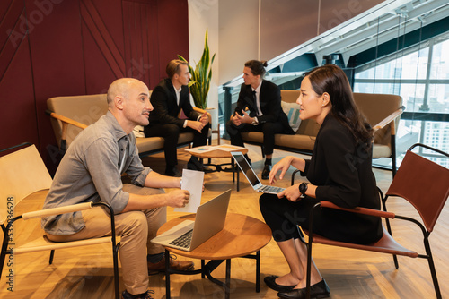 man and woman working together with two businessman discussing at background. businesswoman using laptop in workplace. colleague man and woman working in modern office