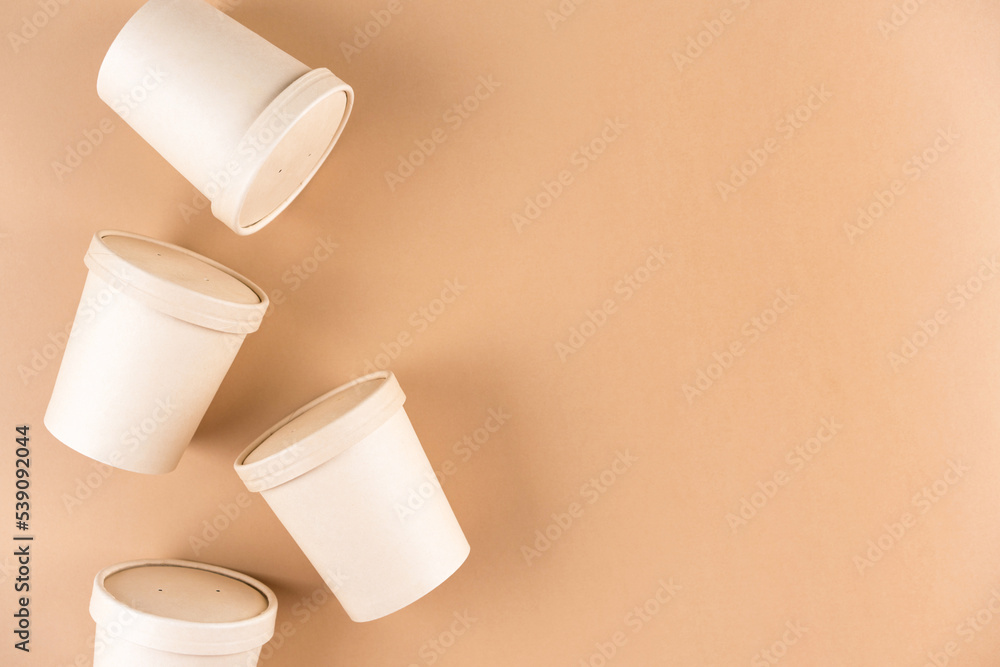 Paper food containers for soup or hot beverages and food take away, cups with paper cap over light brown background with copy space, mockup image. Sustainable food packaging concept Paper food containers for soup or hot beverages and food take away, cups with paper cap over light brown background with copy space, mockup image. Sustainable food packaging concept