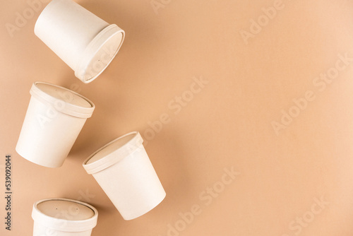 Paper food containers for soup or hot beverages and food take away, cups with paper cap over light brown background with copy space, mockup image. Sustainable food packaging concept