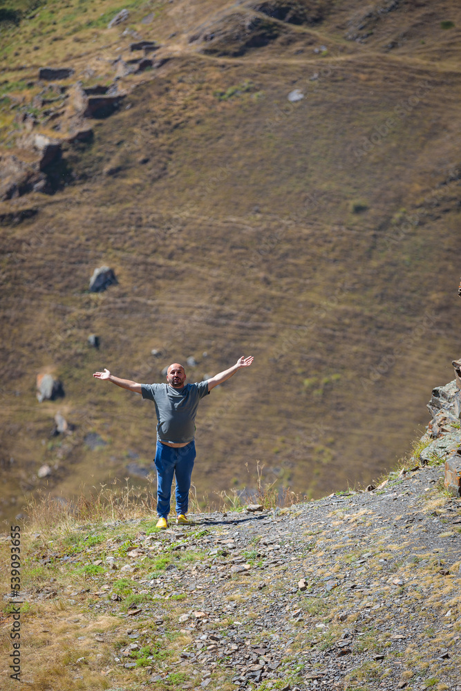A man in the mountains with outstretched arms looks at the camera.