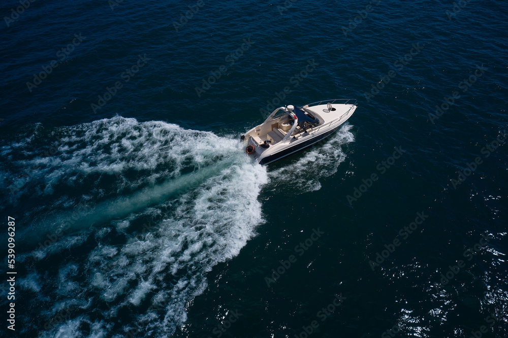 Big boat in motion on the water top view. Luxurious large yacht with people moving quickly on dark blue water making a white trail behind the boat.