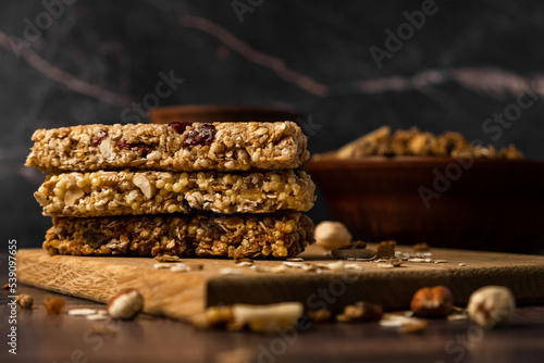 Energy breakfast. Chocolate granola with dried fruits in a bowl, various granola bars on a dark background.