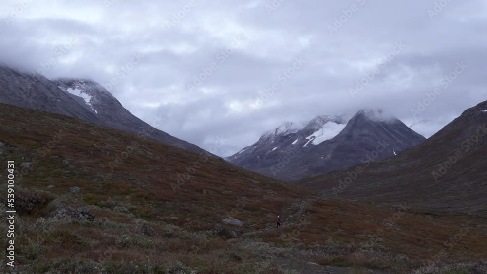 Far view of person hiking during moody morning in valley between wild mountains in Norway Far view of person hiking during moody morning in valley between wild mountains in Norway