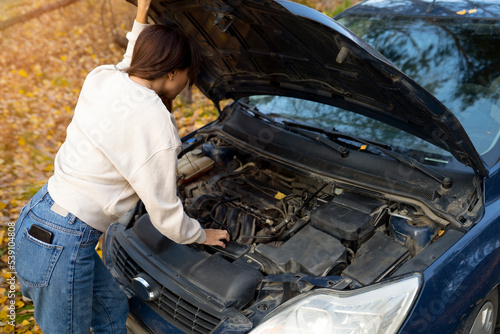 a woman peeks under the hood. a woman repairs a car. car breakdown