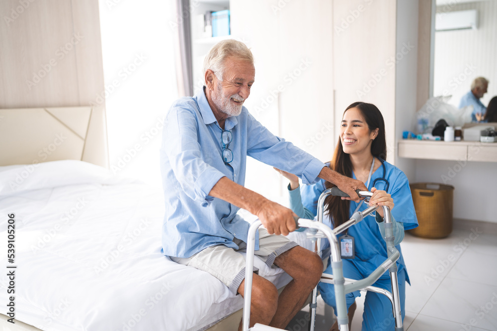 Fototapeta premium Portrait of Asian young nurse helping old elderly disable man grandfather to walk by using walker equipment in the bedroom. Senior patient of nursing home moving with walking frame and nurse support