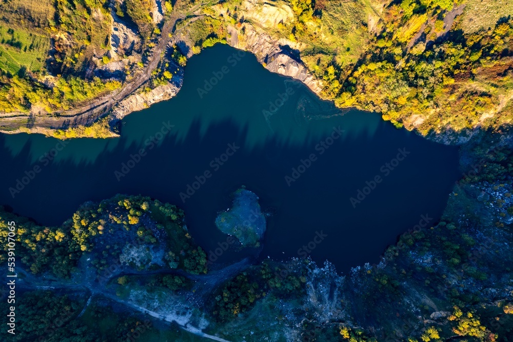 Aerial view of a small lake at sunset, that formed in a former coal mine exploitation, near Resita city, Romania. Captured with a drone, from above, in autumn setting.