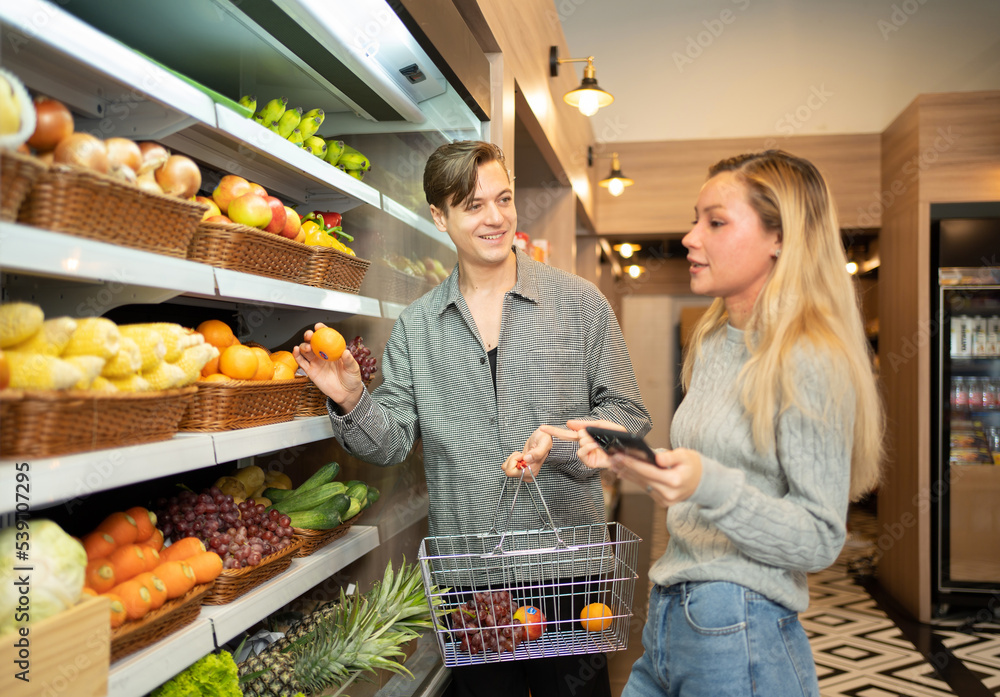 A caucasian couple walking along supermarket, buying fruit and vegetable on grocery products shelves with shopping basket. Food shopping. People lifestyle.