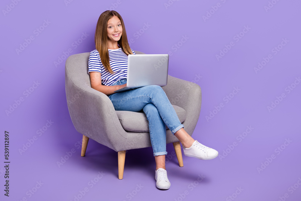 Full length photo of smart intelligent girl dressed striped t-shirt sit in armchair typing on laptop isolated on purple color background Full length photo of smart intelligent girl dressed striped t-shirt sit in armchair typing on laptop isolated on purple color background