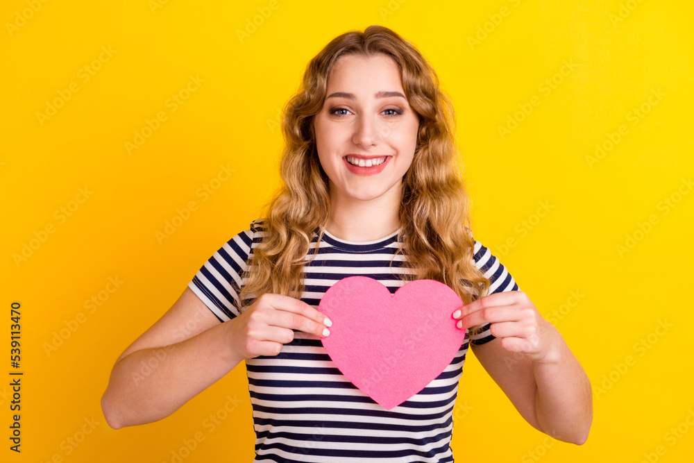 Photo of lovely cheerful girl holding in hands heart form near chest isolated over bright yellow color background Photo of lovely cheerful girl holding in hands heart form near chest isolated over bright yellow color background
