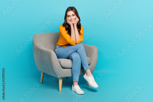 Full length portrait of gorgeous satisfied lad sit chair arms touch cheeks isolated on blue color background