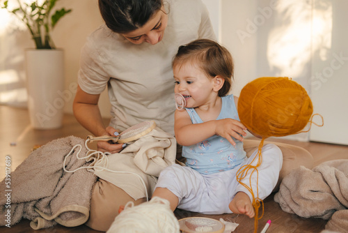 Vászonkép Mother embroidering at the weekend with her younger daughter playing with colorful balls of thread