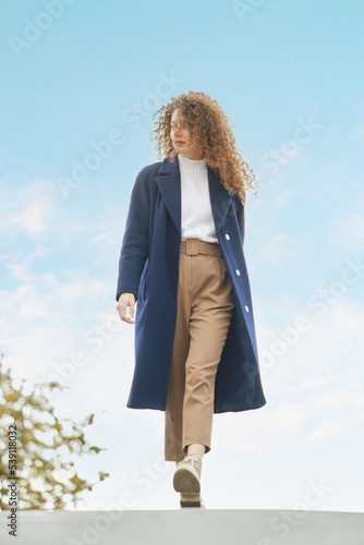 Cute woman in wool coat walks on the bridge in sunny day © boomeart