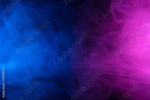 Clouds of colorful smoke in blue and purple neon light swirling on black table background with reflection