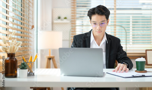 Concentrated male financial advisor using laptop and preparing contract document at office desk.