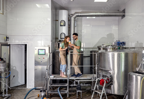 Man and woman working in craft brewery examining quality of the beer.