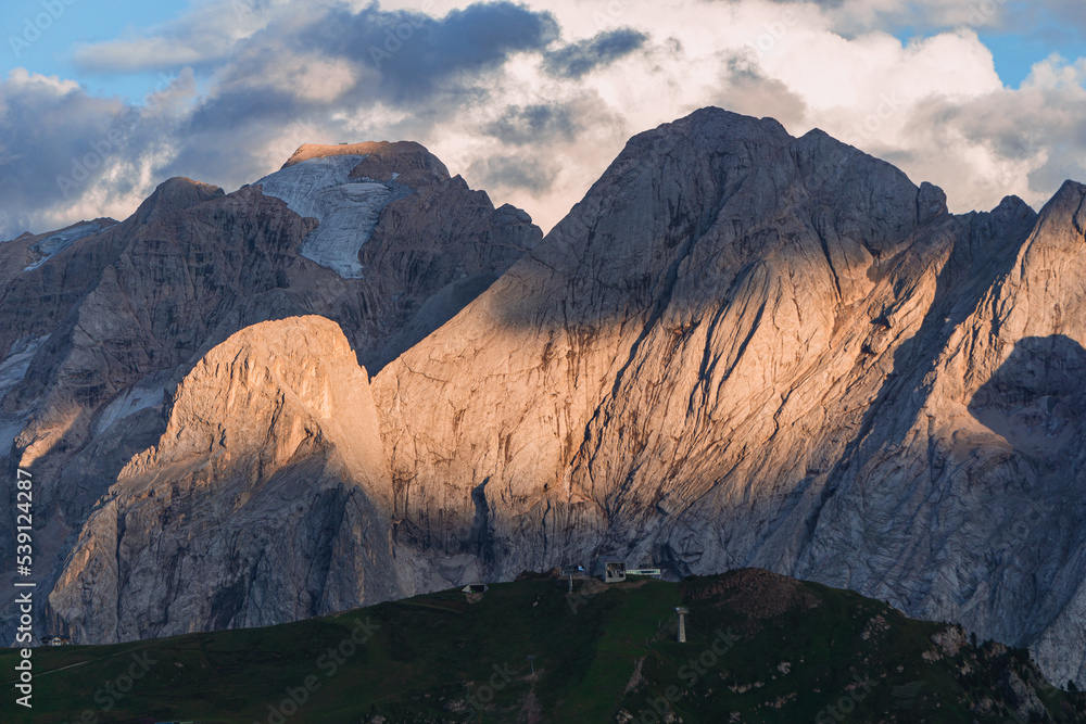 Marmolada, one of the symbolic mountains of the Dolomites and Val di Fassa with the evening lights, near the town of Canaze, Italy - August 2022.