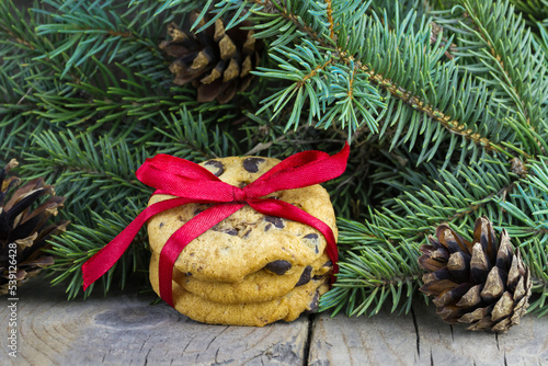 Christmas (New Year) decoration composition. Chocolate chip cookies decorated red bow, fur-tree branches and cones on wooden background