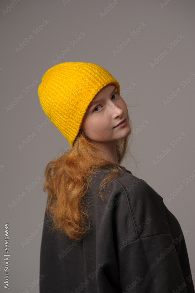 Fototapeta premium young girl model in yellow cap and gray coat isolated on gray background. Product photo mockup for fashion brands and marketplaces, woolen cap, turkish textiles.