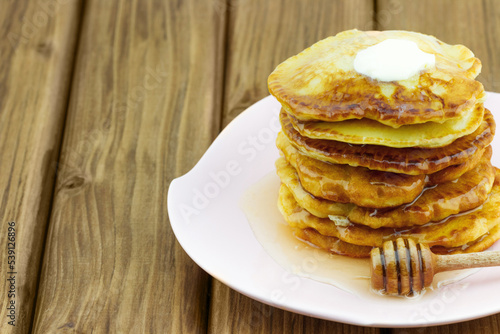 Stack of pancakes with honey and piece of butter on wooden table