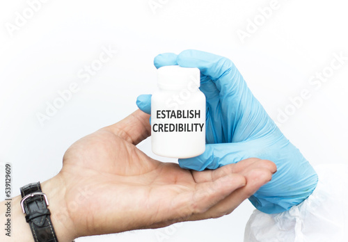 ESTABLISH CREDIBILITY text on a white jar the doctor passes to the patient in the hand on a white background