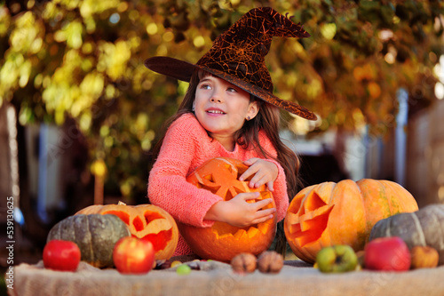 Pretty girl in witch masquerade hat with carver Halloween pumpkins