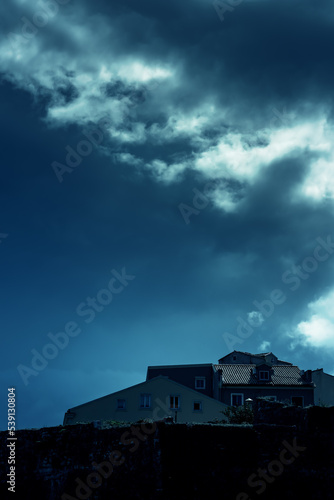 Houses behind a city wall under a dark cloudy sky. © ysbrandcosijn