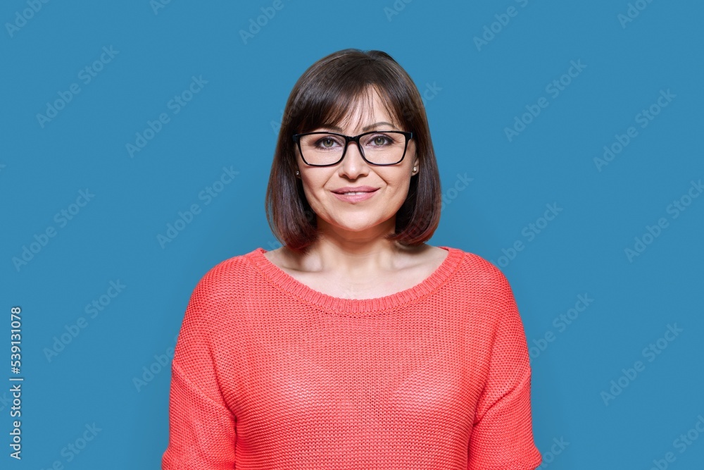 Smiling middle aged female looking at camera on blue studio background