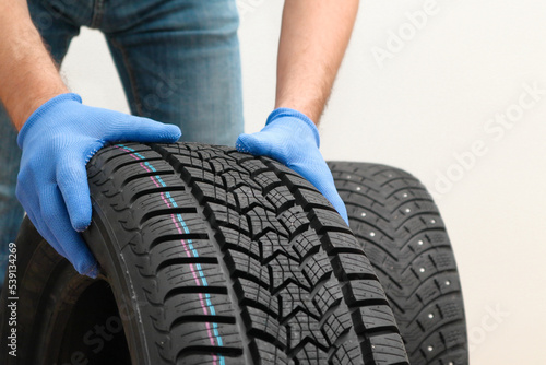 Replacement of winter and summer tires. Mechanic holding a tire at the white background. winter studded tyre, tires replacement