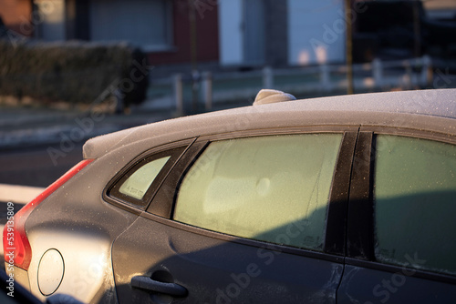 A portrait of the side of a car with frozen side windows during winter. The ice first needs to melt or be removed before the driver can safely start the journey.