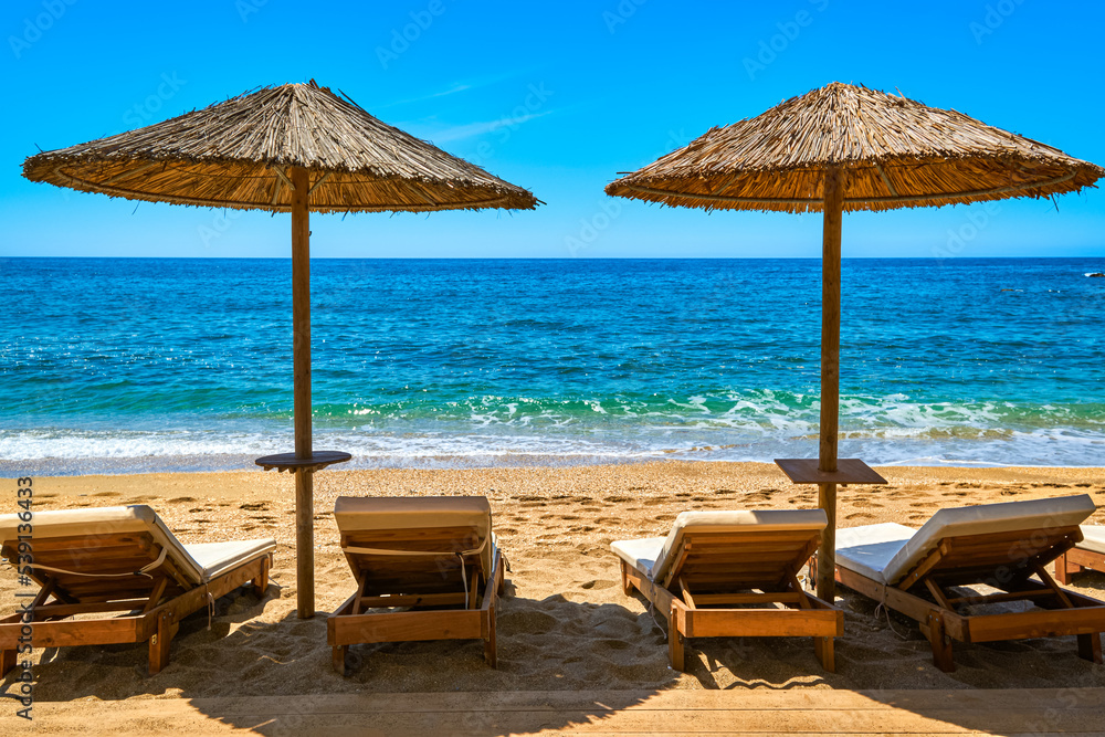 Two sun umbrellas and four sunbeds ready for tourists on sandy beach