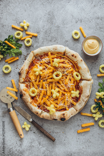 Pizza with cheetos chips and sauce on a gray background.