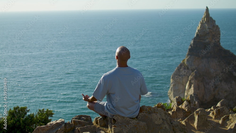 Yoga man practicing meditation at beautiful sea cliff edge in golden sunlight.
