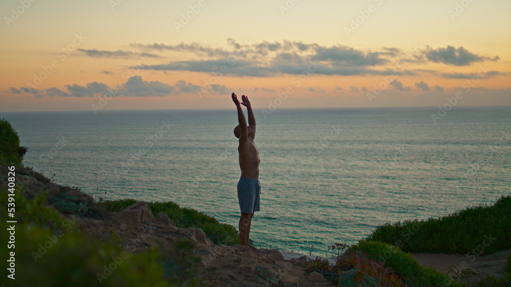 Sunset yogi silhouette training standing head at ocean cliff. Fit man practicing