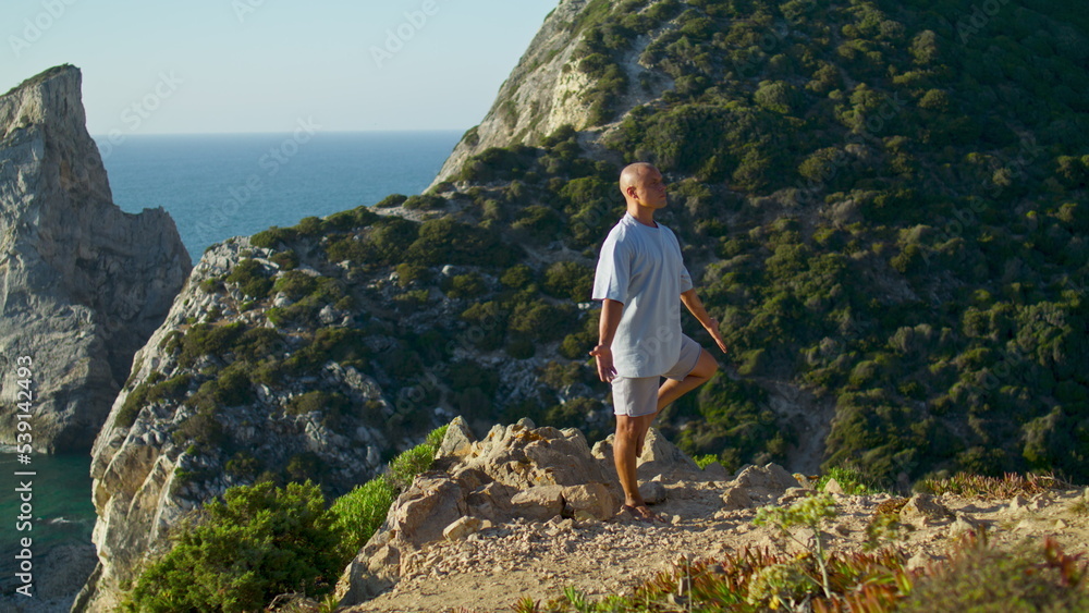 Athlete concentrating yoga asana at beautiful sea cliff edge. Focused man making
