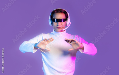 Asian man in white sweatshirt wearing vr glasses and headphone posing hand touching on purple color background. Metaverse and technology concept.