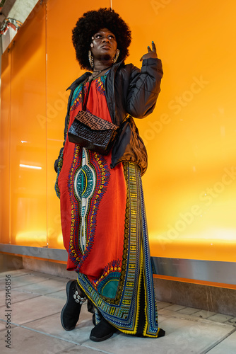 African woman stands against a lighted wall wearing colorful African clothes inside Arlanda Airport Stockholm photo