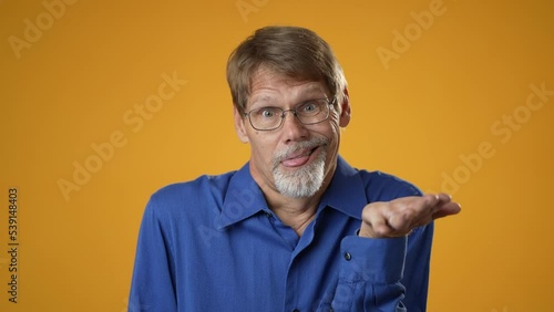 Crazy funny mature man blue shirt making goofy face, fooling faces, childish behaviour. Indoor studio shot isolated on yellow background