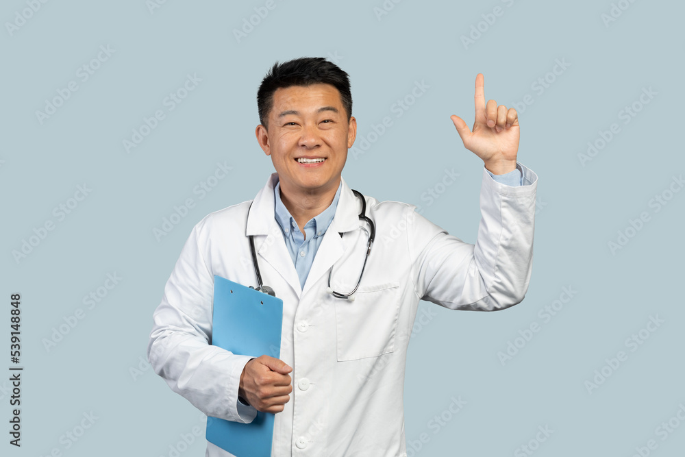 Cheerful middle aged chinese doctor in white coat with stethoscope showing finger up Cheerful middle aged chinese doctor in white coat with stethoscope showing finger up